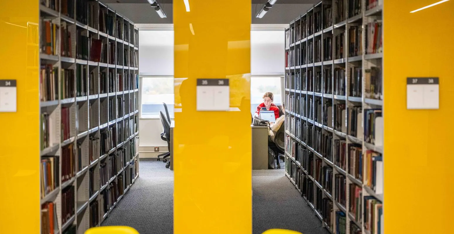 Library image looking through the shelves to a student working at the end