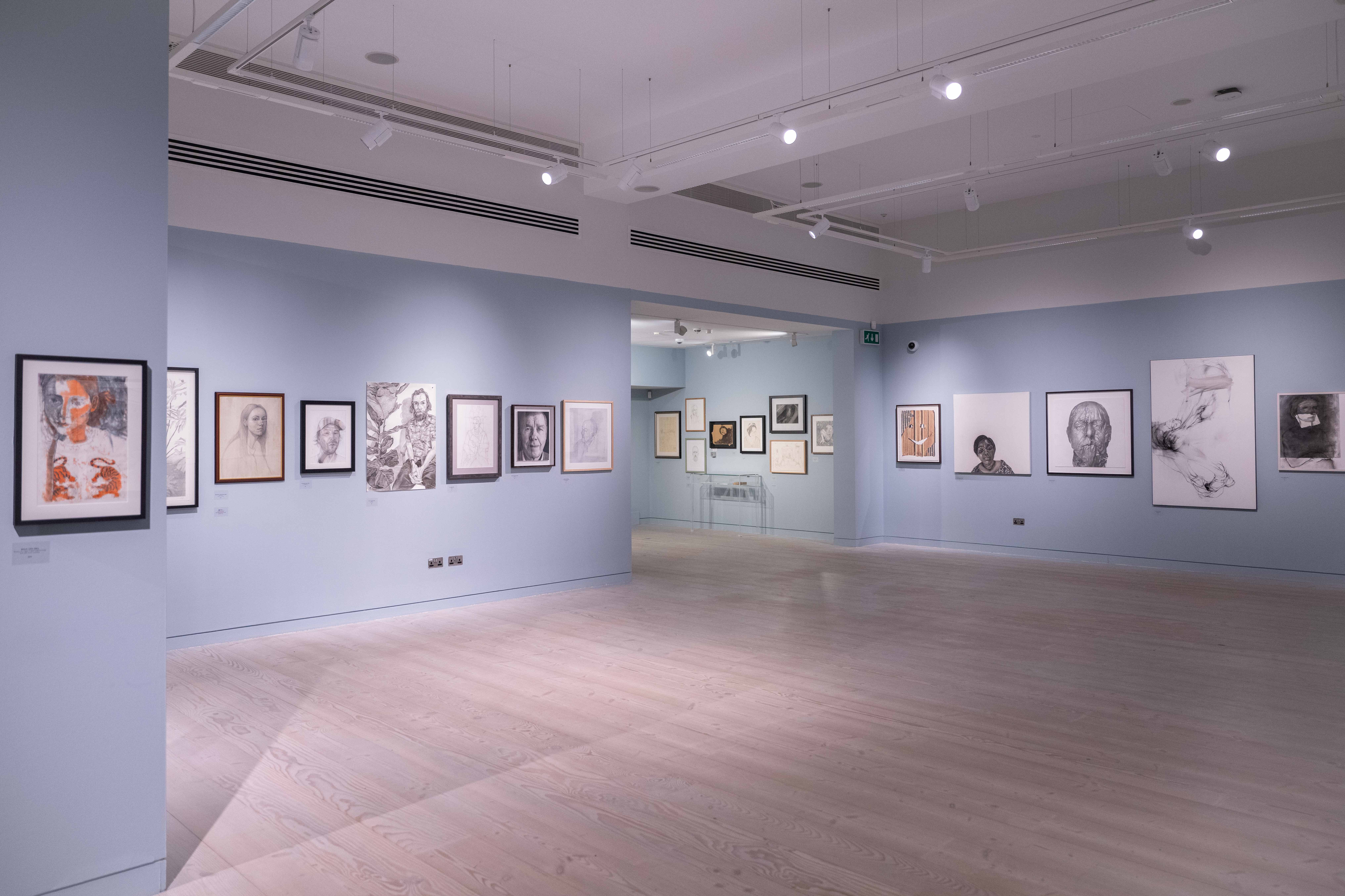 A spacious art gallery with blue walls displays lots of framed sketches and portraits. 