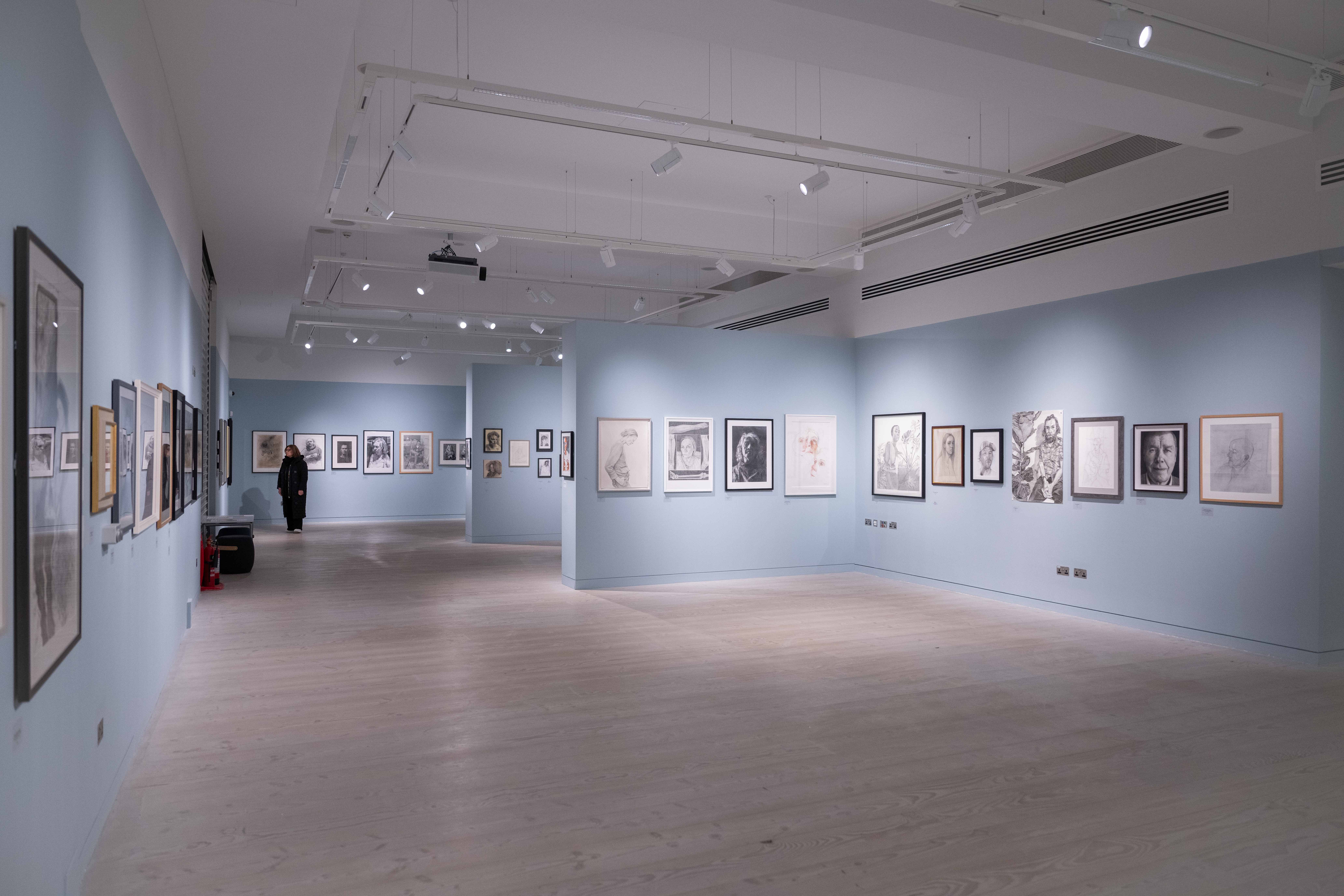 A spacious art gallery with light blue walls displays numerous framed artworks. 